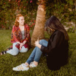 Caitlyn and Rania sitting beneath a palm tree.